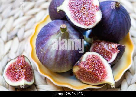 Still life of Fresh Figs lying on a plate with yellow edges, whole and cut into pieces Stock Photo