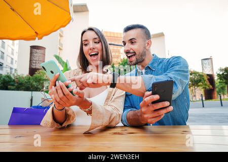 Mele and female having fun sharing media with a mobile phone. Friends watching a smartphone on a coffee shop terrace. Surprised young couple doing online shopping happy to find sales with a cellphone. High quality photo Stock Photo