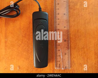 Wired remote control to control the camera on the wooden background and a ruler near Stock Photo