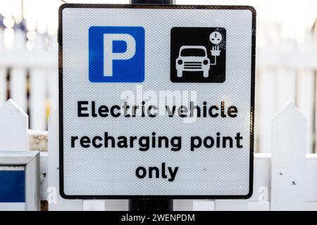 a close up of a charging station and parking sign. The sign is mounted near a fence, and displays the text electric vehicle charging point only. Stock Photo