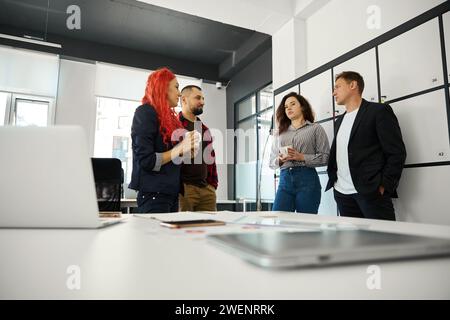 Four colleagues gathering near luggage lockers in office and gossiping Stock Photo