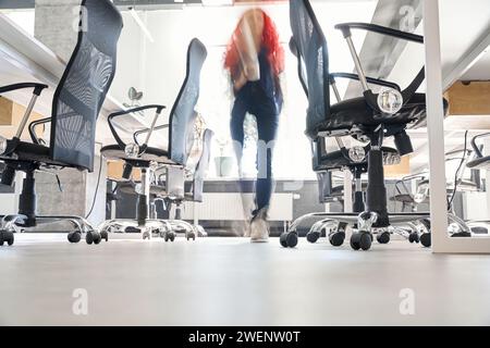 View to woman moving along office room through transparent glass wall Stock Photo