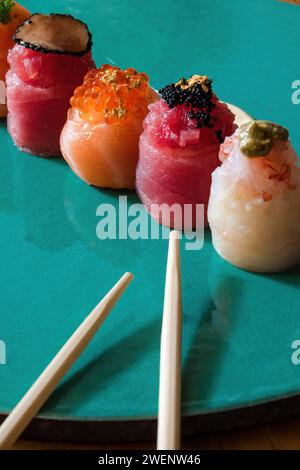 Assorted nigiri sushi, garnished with caviar and gold flakes, presented on a turquoise backdrop. Stock Photo