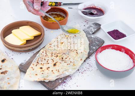 Chef, cook holding spoon by hand, pouring honey on wrapped, grilled pita lying on wooden board. Stock Photo