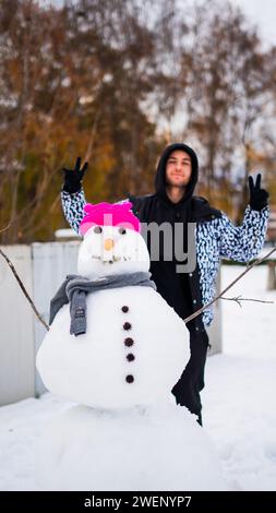 Happy young man with snowman wearing a pink hat and a scarf. Stock Photo