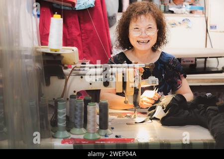 Yilan, Republic of China - October 2, 2023: Portrait of a smiling seamstress and her sewing machine in the city of Yilan, Taiwan. Stock Photo