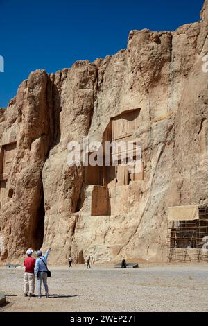 Tourists look at the rock-cut tomb of Artaxerxes I, Achaemenid king (465–425 BC) of Persian Empire. Naqsh-e Rostam Necropolis near Persepolis, Iran. Stock Photo