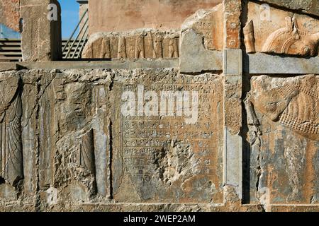 Badly damaged reliefs and cuneiform inscriptions on platform of ruined building in Persepolis, capital of the Achaemenid Empire (550–330 BC), Iran. Stock Photo