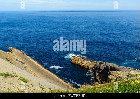 Striking layered rock formations along the rugged coast of Northern Spain with a clear blue sky overhead. Stock Photo