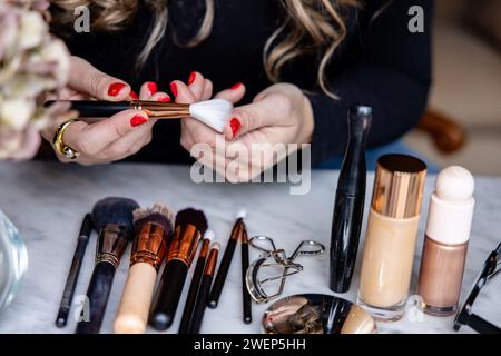 Close-up of a makeup artist's hands as she prepares her brushes and tools, surrounded by various cosmetics on a marble surface. Stock Photo