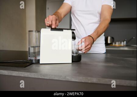 Closeup of a young man preparing freshly brewed coffee in the morning, using a capsule coffee machine. Morning routine. People. Lifestyles. Stock Photo