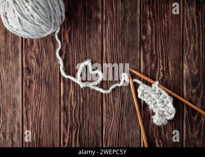 A ball of thread and knitting needles on a wooden background. A heart of thread as a concept of love for needlework and knitting. Stock Photo