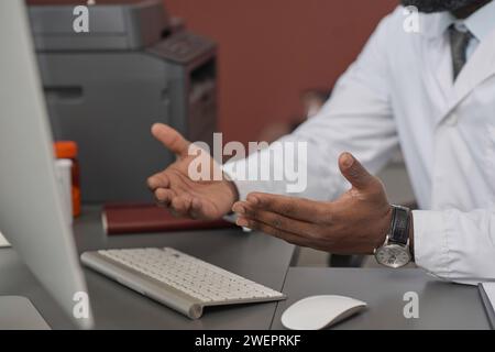 Hands of unrecognizable black doctor in uniform having video call at his workplace in clinic office Stock Photo