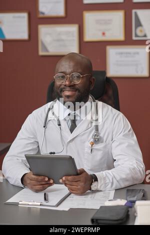 Black medical worker sitting at his desk in clinic with tablet in his hands and looking at camera Stock Photo