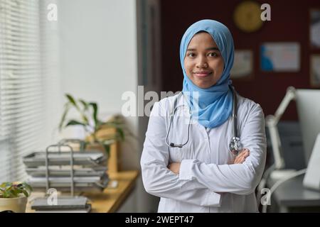 Muslim female physician confidently posing at hospital office and smiling at camera Stock Photo