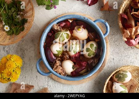 Easter eggs with green leaves attached to them are being dyed with onion peels in a blue pot Stock Photo
