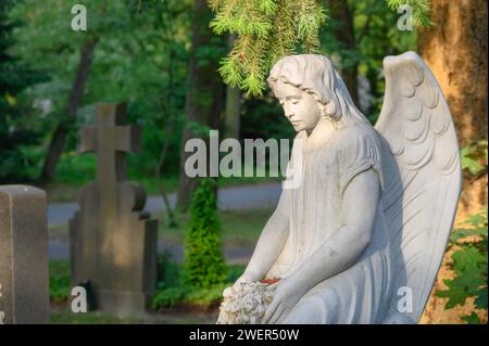 Mourning female statue at the tomb with stone cross in the background Stock Photo