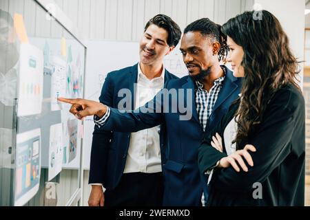 Colleagues meet in the office, using sticky notes on a glass board for brainstorming. This diverse Stock Photo