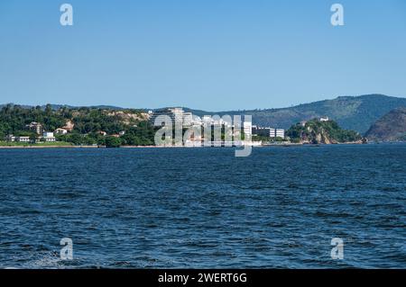 Distant view of Niteroi's Sao Domingos and Gragoata districts coastline as saw from Guanabara bay blue waters under summer afternoon clear blue sky. Stock Photo