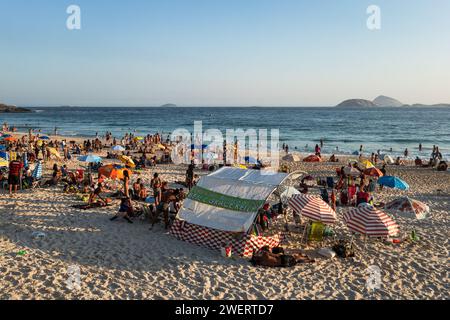 People enjoying some time on the heavily crowded Arpoador beach at Atlantic Ocean blue waters under summer late afternoon sunny clear blue sky. Stock Photo