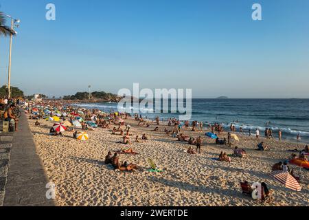 People enjoying some time on the heavily crowded Arpoador beach east end with Arpoador Rock (Pedra do Arpoador) at the end under summer late afternoon. Stock Photo