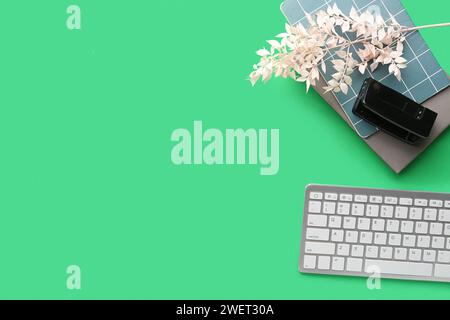 Composition with modern computer keyboard, notebooks and stapler on green background Stock Photo
