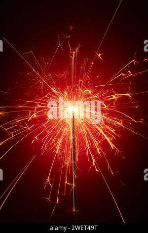 Close up of sparkler is burning, sparks emitting a red glow, standing out against a dark background. Scene of birthday party, happy new year and merry Stock Photo