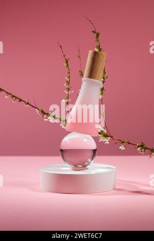 Front view of glass bottle without label, transparent ball and white podium on trendy pink background. Small white flower branch as a highlight. Minim Stock Photo
