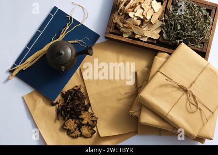 Scene for advertising traditional Chinese medicine with dried herbs on wooden tray, book and medicine package on light background. Top view, copy spac Stock Photo