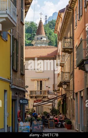 The steeple of the Church of Santa Marta can be seen rising beyond diners eating al fresco on the Via Cavour in Bellano, Lombardy, Italy. Stock Photo