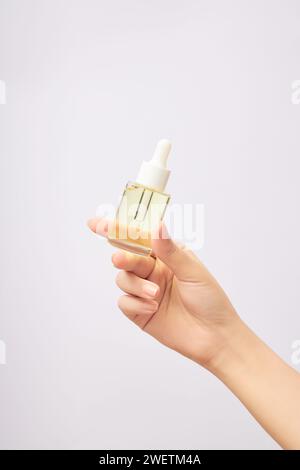 Woman's hand holds mock-up of dropper bottle on white background. Glass bottle without label containing light yellow essence. Space for design, concep Stock Photo