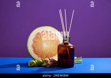 Top view of empty glass bottle, reed diffuser, fresh lemongrass and cut pink pomelo slices on purple background. Mockup scene for products of essentia Stock Photo