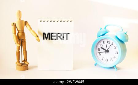 Symbol of merit. Concept text, merit on notepad. Beautiful background with a wooden doll and a clock. Business concept and contributions to the compan Stock Photo