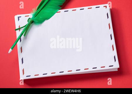 Stack of white greeting envelopes with a pen-shaped feather on a red background, template for designer Stock Photo
