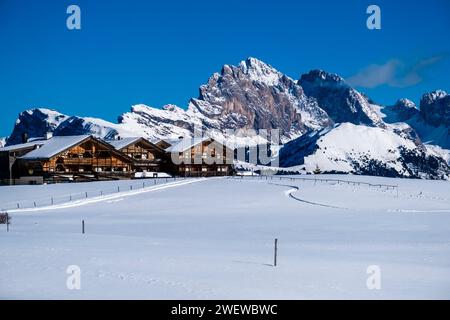 Hilly agricultural countryside with the Alpenhotel Panorama and snow-covered pastures at Seiser Alm, in winter, summits of Odle group in the distance. Stock Photo