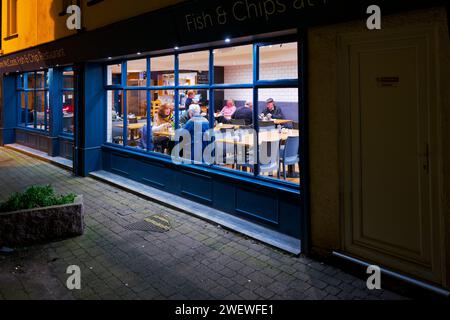 Fish and Chip shop at night photographed from the outside looking in at diners eating fish and chips. Teignmouth, Devon, England. Stock Photo