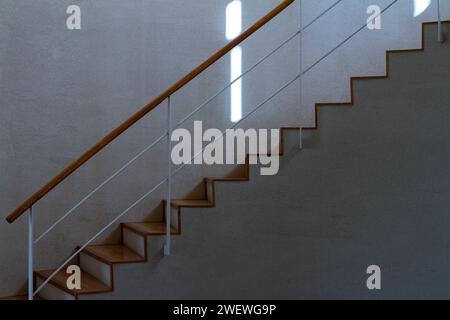 A slightly-curving concrete staircase with a wooden handrail inside an old school building. Kanagawa, Japan. Stock Photo