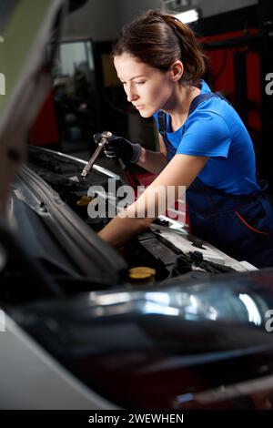 Woman auto mechanic works under an open hood Stock Photo