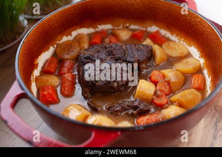 Pot roast with carrots and potatoes slow cooked in red dutch oven, on kitchen table Stock Photo