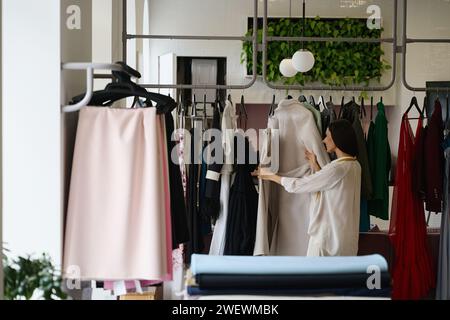 Woman looking at a collection of clothes in a designer studio, woman in comfortable casual clothes Stock Photo