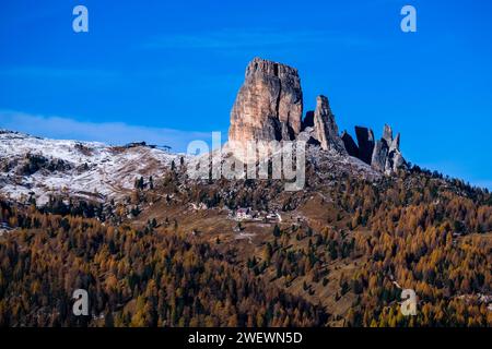 The rock formation Cinque Torri and the mountain hut Rifugio Cinque Torri, surrounded by yellow larches and green pine trees at sunrise in autumn. Stock Photo