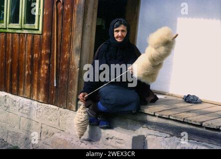 Vrancea County, Romania, approx. 1996. Elderly woman on the porch of her house spinning wool the old-fashioned way. Stock Photo