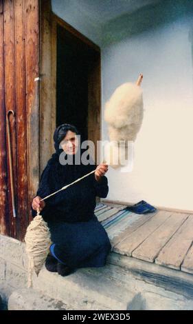 Vrancea County, Romania, approx. 1996. Elderly woman on the porch of her house spinning wool the old-fashioned way. Stock Photo