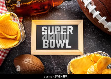 Germany - January 27, 2024: Super Bowl lettering on a board surrounded by snacks, beer and an American football for the Super Bowl. Major sporting event in America PHOTOMONTAGE *** Super Bowl Schriftzug auf einer Tafel umgeben von Snacks, Bier und ein American Football zum Super-Bowl. Großveranstaltung im Sport in Amerika FOTOMONTAGE Stock Photo