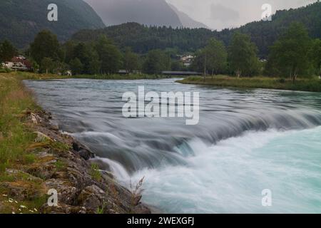 The Loelva River flows through the village of Loen, Norway during an overcast day. It draws its water from the glacier in the mountains around Lovatne Stock Photo