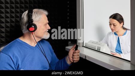 Audiological exam. Audiologist doing hearing check-up to senior man in soundproof audiometric booth. Hearing loss treatment Stock Photo