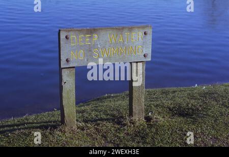 A wooden sign with carved lettering warning Deep Water No Swiming by the Needham Lake Needham Market Suffolk Stock Photo