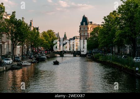 Evening Calm on Amsterdam's Canals: A Graceful Mingle of Historic Architecture and Leisurely Boating Stock Photo