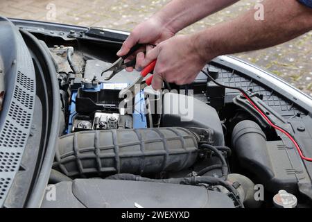 Hands With Cables Charging Up A Car Battery In Engine Bay Stock Photo