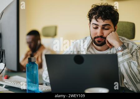 Handsome male person staring at his lap top as he struggles to find a solution for his problem at work. Stock Photo